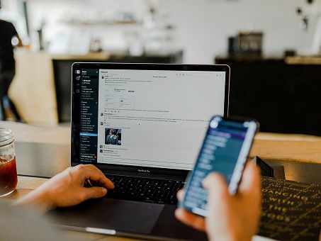A developer watching a running build on a laptop with a phone in hand